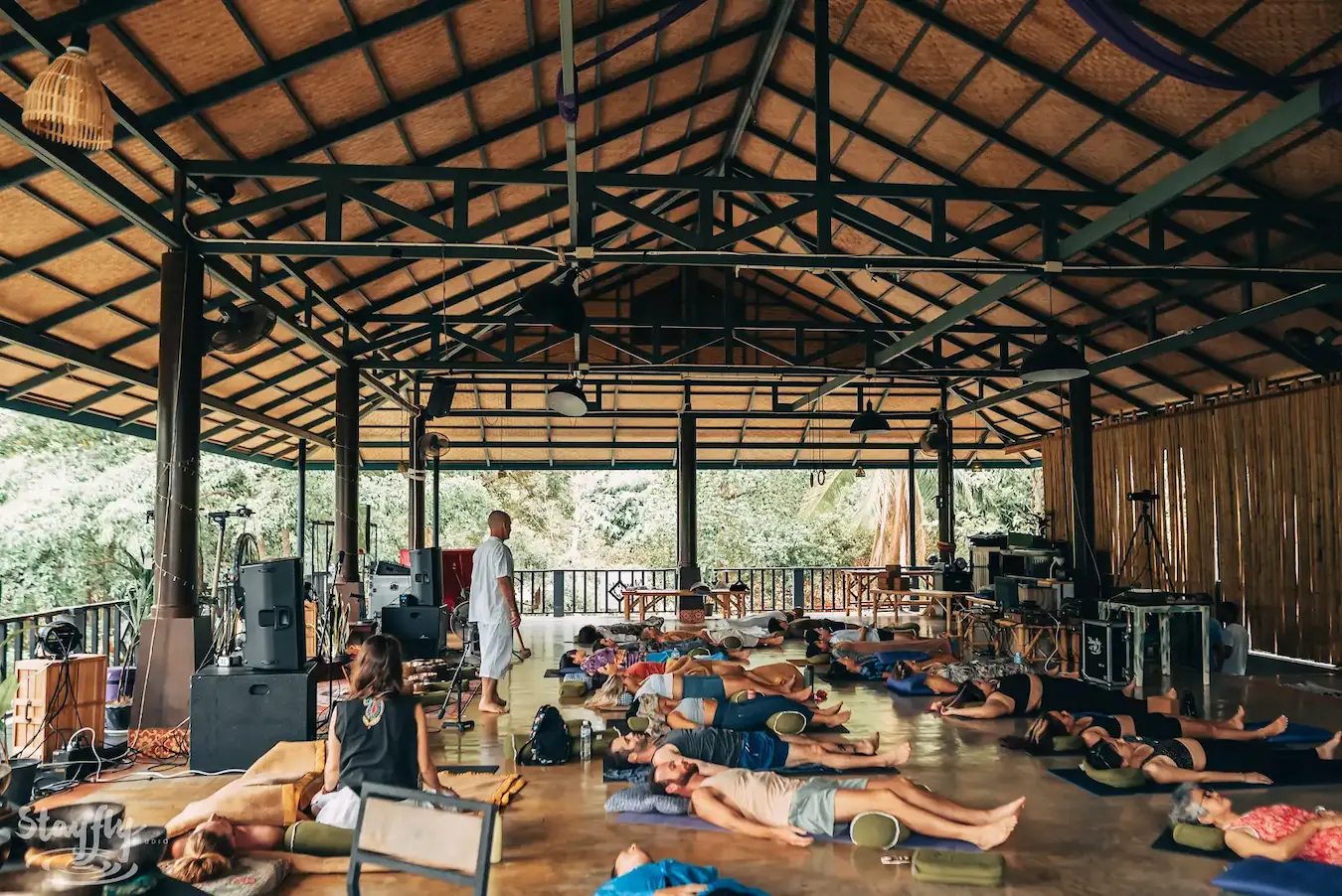 The pavilion by daylight, participants lying on mats beneath the gongs and the palms.