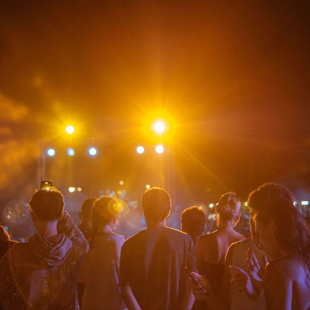 A crowd faces a stage under warm orange lights at night.