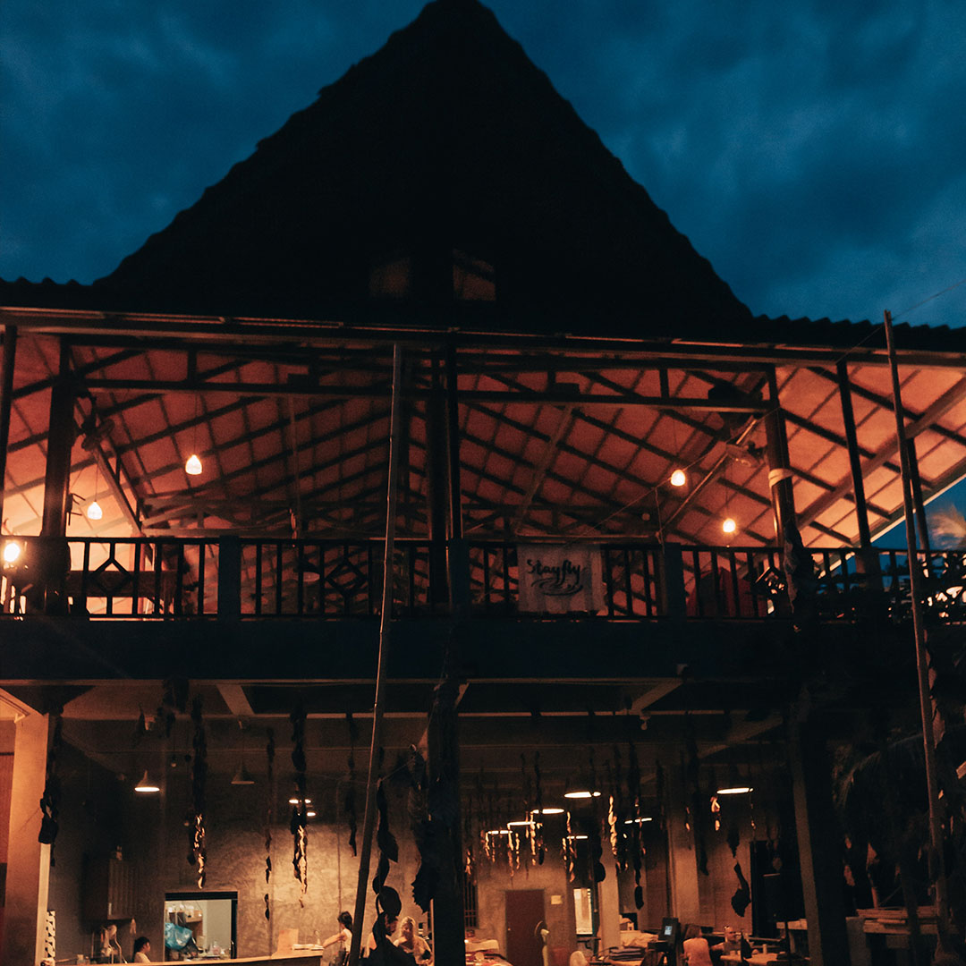 The open sided hall at blue hour, lights on inside and the sky darkening above the roof.